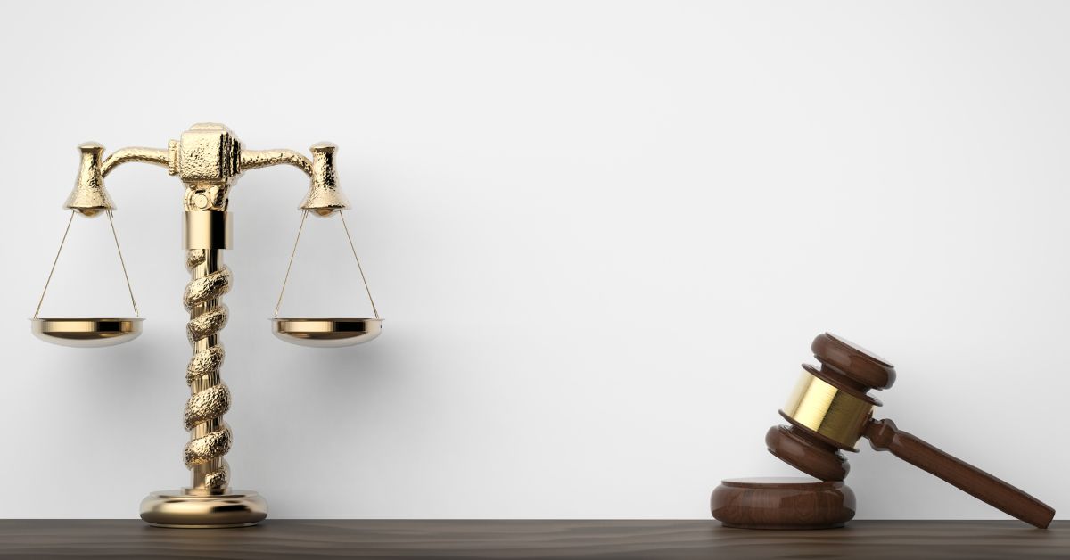 A golden scale of justice and a wooden gavel resting on a dark surface, symbolizing legal balance and authority in a courtroom setting.