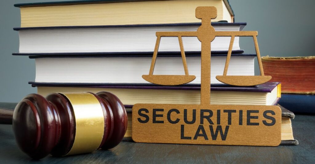 A gavel rests on a stack of books, with one book prominently labeled "SECURITIES LAW." A small scale of justice sits atop the books, symbolizing legal balance.
