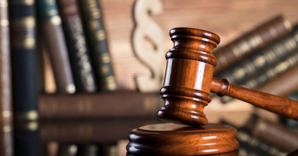 A wooden gavel resting on a stand, with law books and a scales of justice symbol in the background, representing legal authority and justice.
