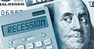 An image featuring a calculator displaying the word "RECESSION" overlaid on a partial view of a U.S. hundred-dollar bill with Benjamin Franklin's portrait.