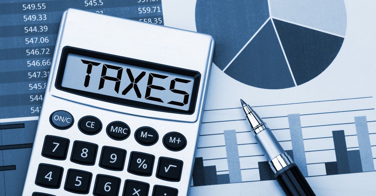 aCalculator displaying "TAXES" with a pen and financial charts in the background.