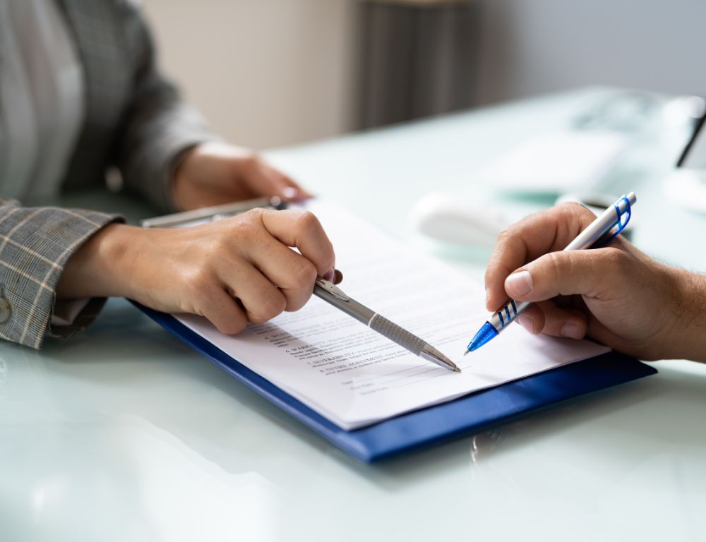 wo hands holding pens, actively drafting or reviewing an employment contract on a clipboard for a deal.