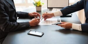 Two people in suits signing documents indicating a business agreement or contract signing.