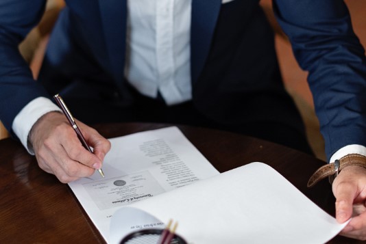 Two individuals in suits reviewing and signing documents.