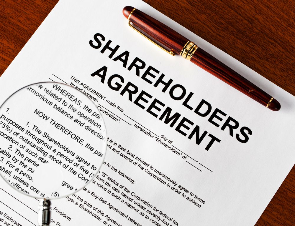 A document titled "Shareholders Agreement" with a pen resting on top, placed on a wooden surface.