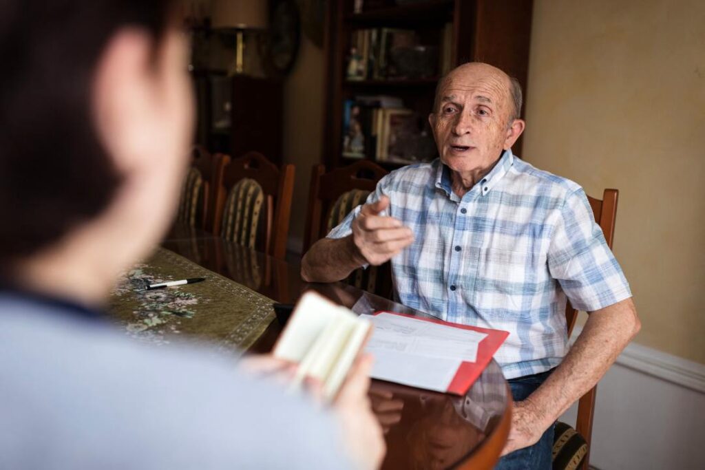 Elderly man discussing paperwork with another person about the legal and financial implications of canceling a franchise agreement in Canada.