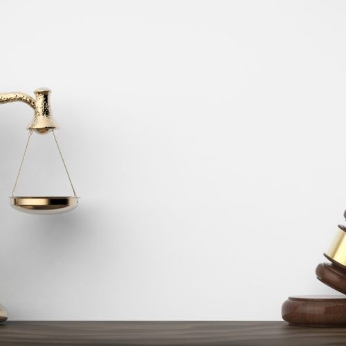 A golden scale of justice and a wooden gavel resting on a dark surface, symbolizing legal balance and authority in a courtroom setting.