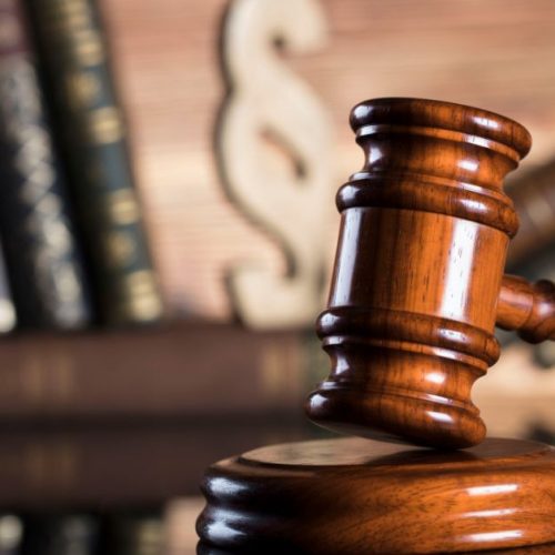 A wooden gavel resting on a stand, with law books and a scales of justice symbol in the background, representing legal authority and justice.