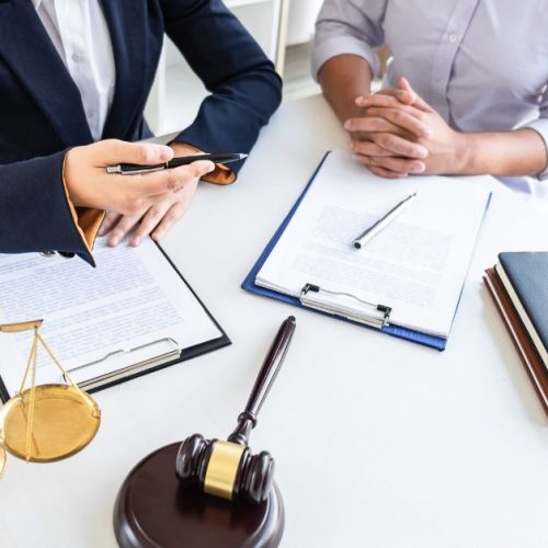 Two professionals reviewing documents with a gavel and scales of justice on a table, symbolizing legal considerations for business expansion across Canada.