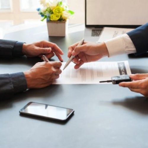 Two people in suits signing documents indicating a business agreement or contract signing.